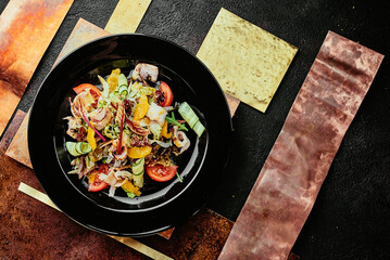 salad with ham, orange slices, tomato, cucumber and lettuce leaves in a black plate on a copper background. 