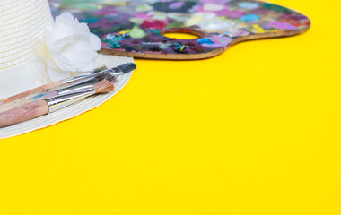 Colourful painting palette, brush, women straw hat on yellow background. Painting concept.