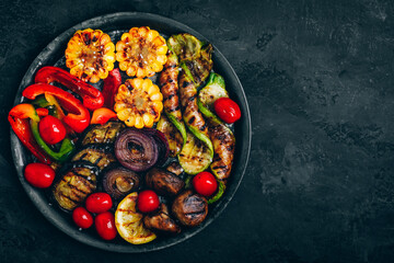 Grilled vegetables in bowl on dark stone background, top view.
