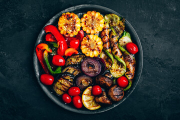 Grilled vegetables in bowl on dark stone background, top view.