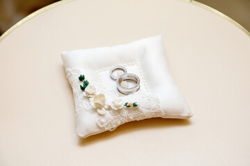 two silver wedding rings lying on a white pillow decorated with lace and flowers
