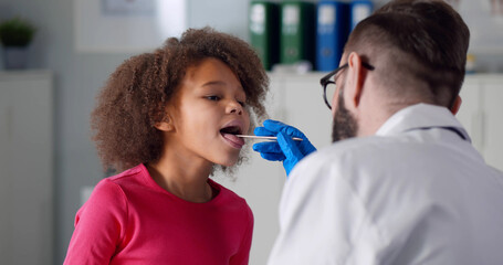 Children doctor examining little patient throat in clinic office