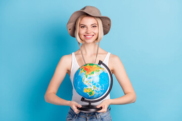 Photo of attractive happy young woman tourist hold hands globe wear hat isolated on blue color background