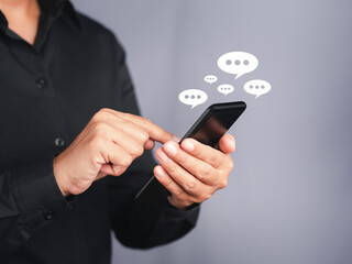 Businessman using a smartphone with an conversation icon while standing with a gray background. Space for text. Communication and technology concept