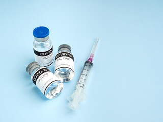 COVID-19 vaccine in glass bottles with a syringe placed on a light blue background. Vaccine for immunization, and treatment from coronavirus infection. Top view. Concept of medical and healthcare