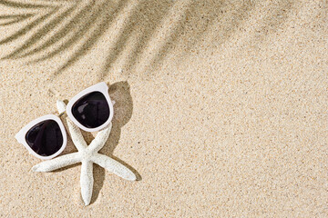 Fototapeta na wymiar Starfish and white sunglasses on natural sand background, copy space