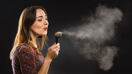 makeup artist with the beauty brush blows on powder