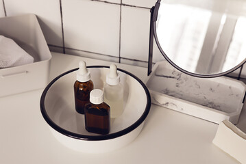 Various glass bottles for skincare cosmetics and spa next to a marble mirror on bathroom white tile background. Zero waste natural cosmetics on a dressing table.