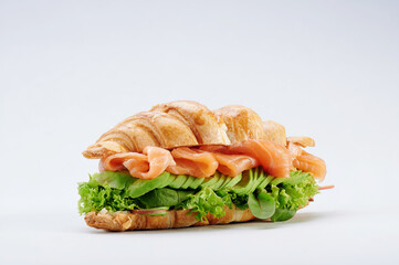 Beautiful croissant with salmon, cheese, avocado, lettuce isolated on a white plate. healthy breakfast. close up