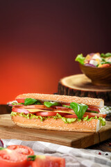 Baguette sandwiches with Ham, sliced cheese, tomatoes and fresh lettuce on wooden cutting board. Dark red background. Space for text. Close up
