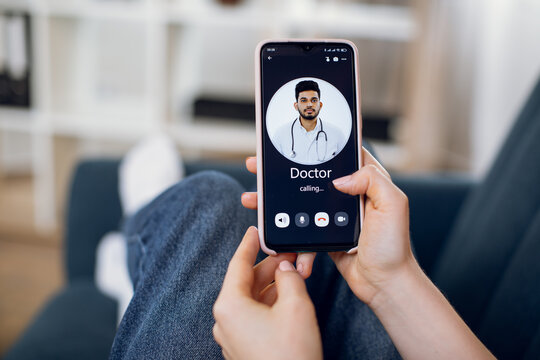 Close-up Back View Of Female Patient Hands, Using Smart Phone And Calling To Her Doctor, Young Indian Man. App For Remote Medical Service.