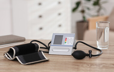 Modern blood pressure monitor and glass of water on wooden table indoors