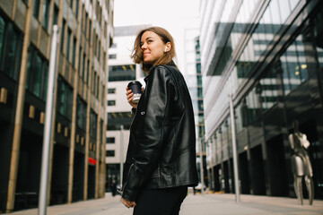 Young pretty girl listening to music in the big city. girl in a leather jacket with headphones...