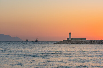 Lighthouse and boats in Aegean Sea at dramatical sunset view in Kusadasi, Aydin, Turkey.
