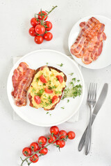 Scrambled eggs with microgreen, bacon and tomato slices on bread