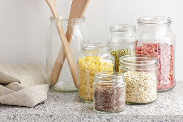 Variety of cereals, grains, pasta, seeds in glass jars uncooked on white kitchen background, closeup, zero waste, eco friendly, balanced diet food, healthy clean eating concept