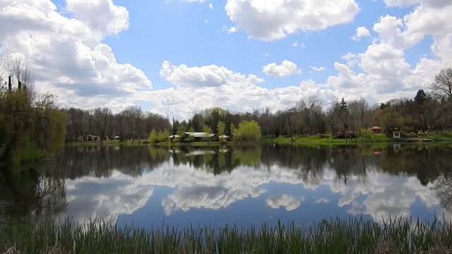 Serene landscape scene with the lake of the Constantin Stere park  , a recreational area near Ploiesti City , Romania at the beginning of spring season , calm day and puffy white clouds reflected on t
