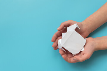 Child hands holding white paper turtle on blue background
