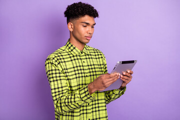 Portrait of handsome focused brunet guy holding in hands using device reading isolated over violet purple color background