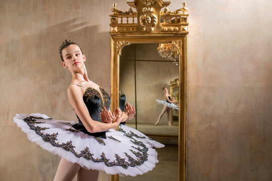 young ballerina in a white tutu poses near beautiful old mummer in vintage interior, reflecting many times