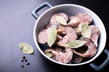 Slices of lightly salted mackerel fish with allspice and bay leaf on a black wooden table.