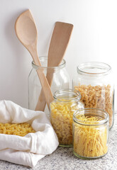 Variety of italian pasta in glass jars uncooked on white kitchen background, closeup, zero waste, eco friendly, balanced diet food, healthy clean eating concept