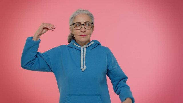 Elderly granny woman showing bla-bla-bla nonsense gesture with hands and rolling eyes, gossips, empty promises, blah concept. Lier. Senior old grandmother on pink background. People lifestyle emotions