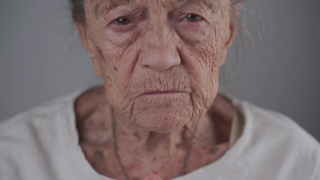 Dental concept. Elderly female 90 years old inserts denture. Senior woman gray hair using dental prosthesis on gray background. Old patient fitted artificial jaw in studio. Flexible nylon denture