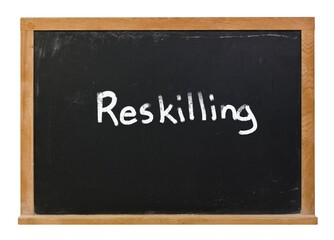 Reskilling written in white chalk on a black chalkboard isolated on white