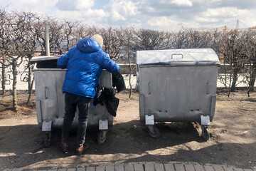 young lonely Caucasian man looking for food and valuables in the trash can. poverty and unemployment during the economic crisis.