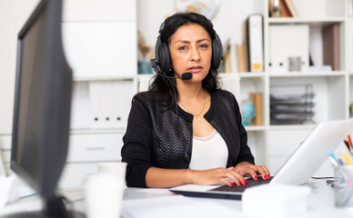 Portrait of experienced female customer support phone operator with headphones during work in call center