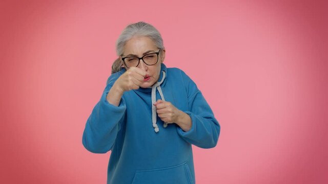 Funny elderly good-looking granny woman trying to fight at camera, shaking fist, boxing with expression, punishment. Senior old grandmother isolated on pink background. People lifestyle emotions