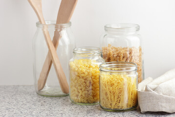 Variety of italian pasta in glass jars uncooked on white kitchen background, closeup, zero waste, eco friendly, balanced diet food, healthy clean eating concept