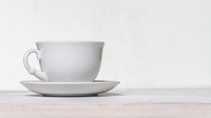 White cup and saucer on a white wooden table, side view