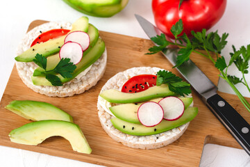 Rice cake sandwich with cheese cream, avocado, tomato, radish and spices. A healthy dietary snack