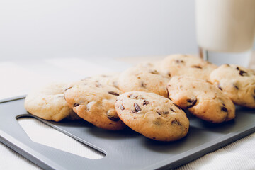 Chocolate chip cookies on gray and wooden table and glass of milk in the background