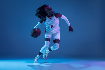 Beautiful african-american female basketball player in motion and action in neon light on blue...