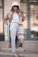 woman in fashionable clothes walks through the city. Coat and headwear