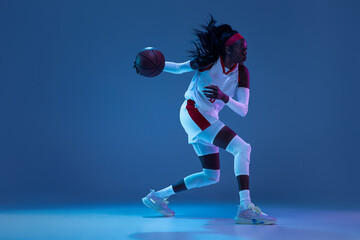 Beautiful african-american female basketball player in motion and action in neon light on blue...