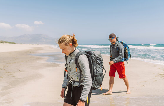 Father with teenager son with backpacks walking by the sandy seaside beach during Lycian Way trekking walk. Famous Likya Yolu Turkish route. Active happy family people vacation time concept image. 