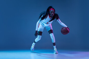 Beautiful african-american female basketball player in motion and action in neon light on blue background. Concept of healthy lifestyle, professional sport, hobby. © master1305