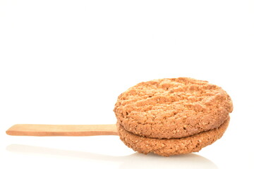Two fragrant dark brown, oatmeal cookies with a wooden spoon, close-up, isolated on white.
