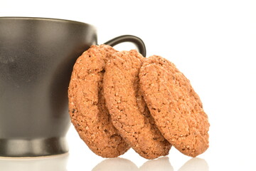 Three fragrant dark brown oatmeal cookies with a black ceramic cup, close-up, isolated on white.