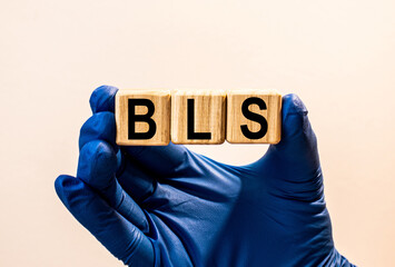 The word BLS which is made from wooden cubes. Hands in a blue glove. Isolated on WHITE background