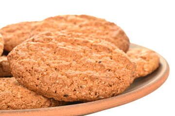 Three fragrant dark brown, oatmeal cookies on earthenware, close-up, isolated on white.