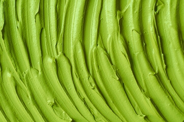 Green cosmetic clay (cucumber facial mask, avocado face cream, green tea matcha body wrap) texture close up, selective focus. Abstract background with brush strokes.