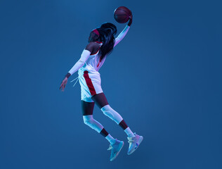 Fototapeta na wymiar Beautiful african-american female basketball player in motion and action in neon light on blue background. Concept of healthy lifestyle, professional sport, hobby.