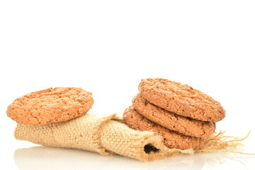 Several fragrant dark brown, oatmeal cookies on a jute napkin, close-up, isolated on white.