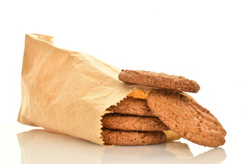 Several fragrant dark brown, oatmeal cookies in a paper bag, close-up, isolated on white.