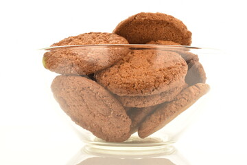 Several fragrant dark brown, oatmeal cookies in a glass dish, close-up, isolated on white.